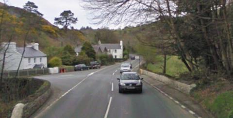 The Junction at Ballig Bridge. There are white houses on the left and trees on the right.