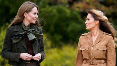 First Lady Melania Trump and Catherine, Princess of Wales talk to each other while walking in a garden.