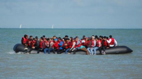 A large inflatable boat is packed with people wearing red life jackets. 
