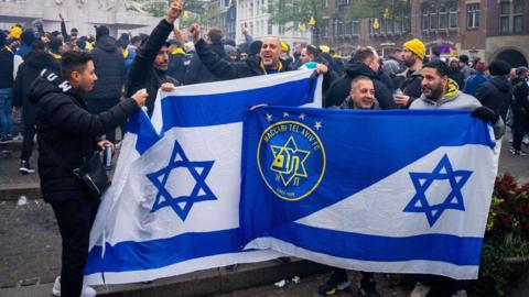 Supporters of Maccabi Tel Aviv hold flags at Dam square ahead of the Europa League football match between Ajax and Maccabi Tel Aviv, in Amsterdam on November 7, 2024. (P