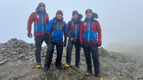 Matt and the three fell top assessors stand on the rocky top of a Helvellyn, surrounded by fog