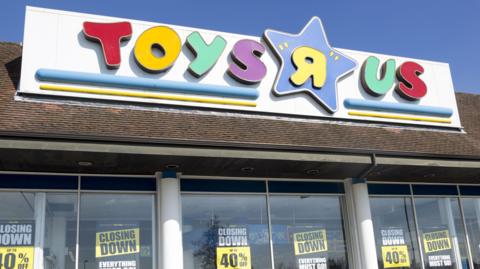 The colourful Toys R Us sign positioned above shop windows in which there are closing down signs