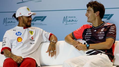 Lewis Hamilton and George Russell smile while talking to each other at a Miami Grand Prix news conference