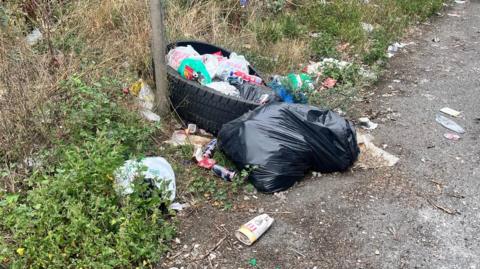 A black bin bag, a tyre, and rubbish on the ground.