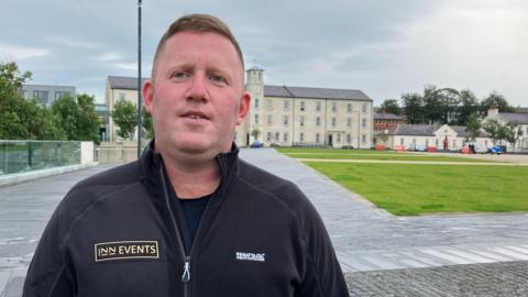 Stephen Doherty stands in front of Ebrington Square. He has a black fleece and short sandy coloured hair