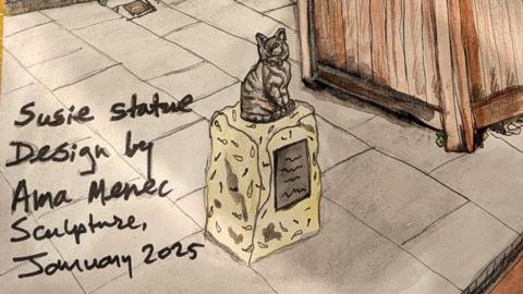 An ink and pen sketch of the cat statue. The tabby cat is sitting on a low stone plinth on the pavement next to a wooden planter. A handwritten note reads: Susie statue design by Ama Menec Sculpture, January 2025.
