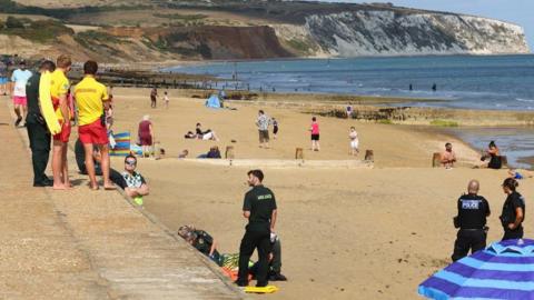Sea wall in Sandown with lifeguards standing at the top and police and paramedics seen on the sand below.