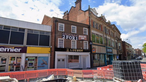 A terraced red brick building with a golden sign that states R Lounge in front