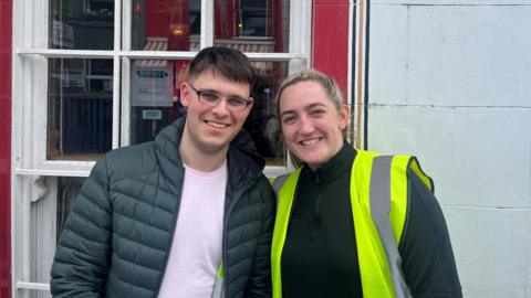 a man in a dark green puffa-style jacket and a woman in a high-viz jacket