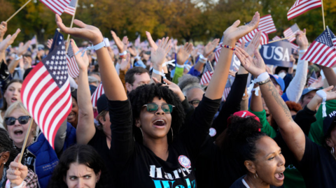 A woman clapping in a crowd with people holding American flags