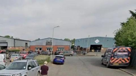 Google Streetview image of three industrial buildings made of brick and corrugated roofs with cars and vans in the foreground