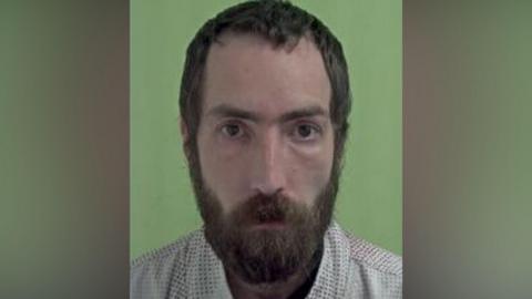 Police mugshot of Hamon, who has short dark brown hair and a full beard.