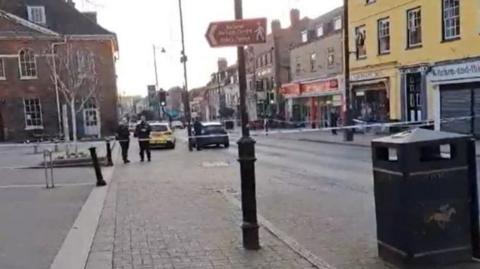 High Street in Newmarket with police cars, police officers and police tape across the road.