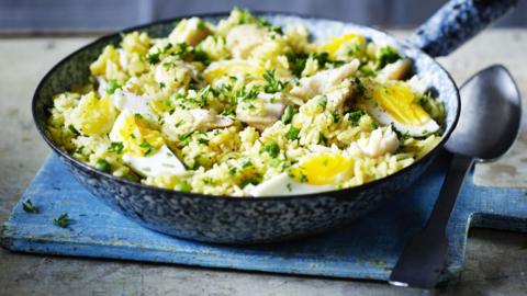 A bowl of yellow rice mixed with boiled eggs, white fish and green garnish.