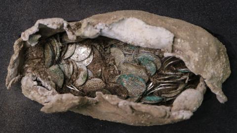 A close-up of a hoard of silver coins inside a beige pasty-shaped pouch