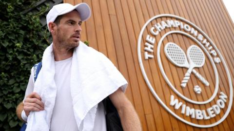 Andy Murray walks next to a sign for Wimbledon at the All England Club