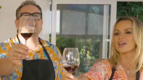 A man, Alan Carr, and a woman, Amanda Holden, toast with wine glasses holding red wine