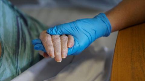 A gloved hand holding an elderly person's hand