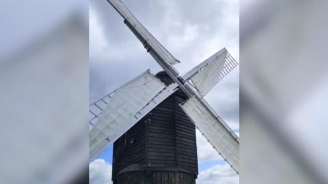 The windmill has a wooden frame which has been painted black. The rotating arms have been painted white and now have material wrapped around them to make them rotate in the wind.