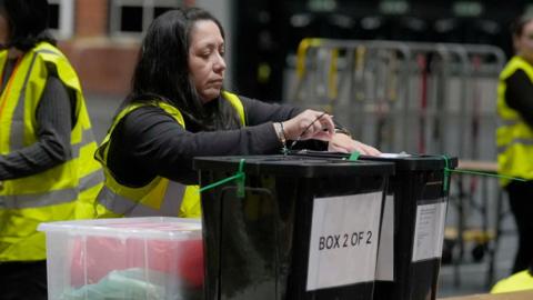 Boxes of vote arriving at count with woman in hi-viz opening them