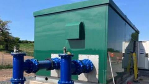 A large green metal container with two large blue metal taps coming out of the side. 