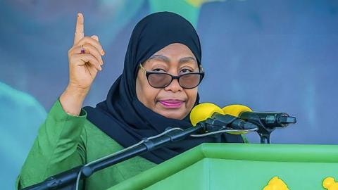 Tanzania President Samia Suluhu Hassan, in green garment and black head scarf, speaking to a microphone at a podium