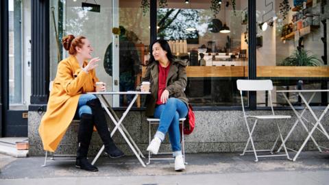 Woman gesturing while talking with female friend outside coffee shop