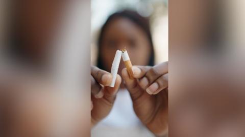A woman breaks a cigarette in half.