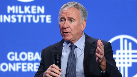 Ken Griffin speaks into a microphone at a conference against a blue backdrop.
