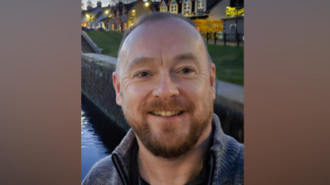 Jim Fleming, wearing a blue jumper, smiles in a photo by a canal