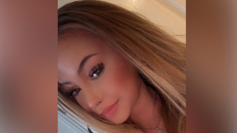 A slanted, selfie image of a young woman with long blonde hair. She is wearing a necklace and looking directly into the camera. 