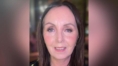 Diane Jones has long brown hair and is smiling at the camera. She is wearing earrings. 