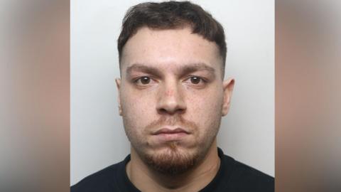 Mugshot of Mohammed Kamal wearing a black t-shirt. He has short brown hair and a red goatee beard. 