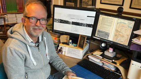 Adrian Webb with his computer and research