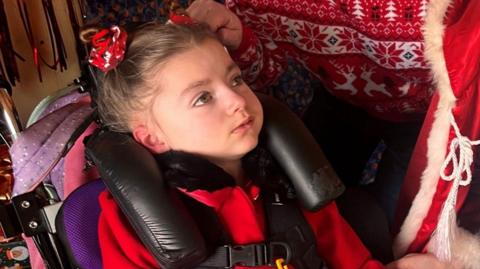 A girl wearing red is looking away from the camera. Someone else at the top of the photo is wearing a red Christmas jumper.