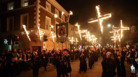 Thirteen burning crosses are carried through the crowded streets of Lewes by people wearing monastic habits.