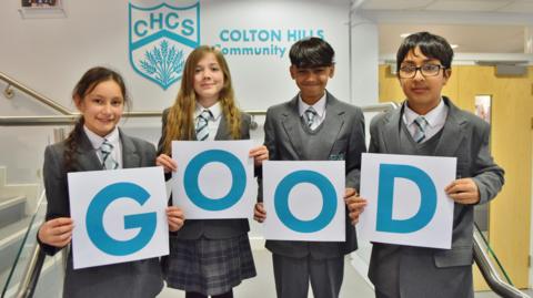 Four children holding signs which spell out 'Good' 