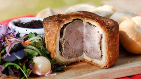 A pork pie with a slice taken out of it 