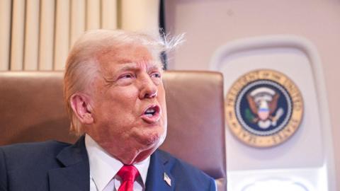 Trump speaking to reporters on Air Force One prior to the Super Bowl, a presidential seal is in the background