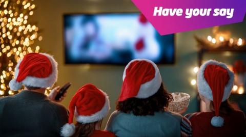 A family wearing Christmas hats and watching TV.