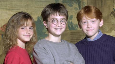 A picture of the three Harry Potter child actors, pictured in the early 2000s. All three are smiling and looking at the camera. 
