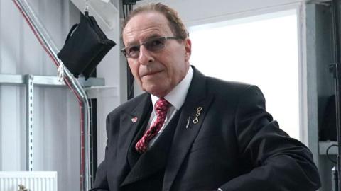 Peter James in a dark suit and red tie.