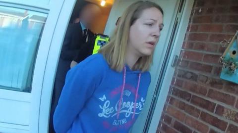 Screen grab taken from body worn camera footage issued by Cheshire Constabulary of the arrest of Lucy Letby. She is wearing a blue Lee Cooper hoody and has shoulder length blonde hair. 