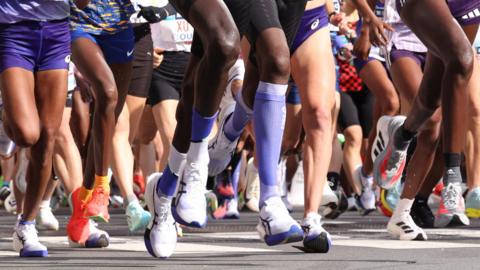 A picture of a crowed of runners where you can only see the bottom half of their body as they run in a marathon. 