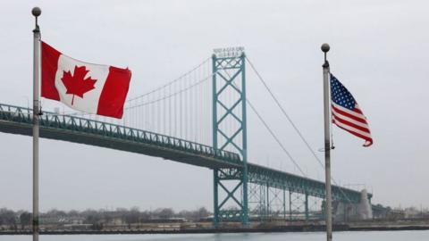 The Ambassador Bridge between Windsor, Canada and Detroit, Michigan, with Canadian and US flags in the foreground