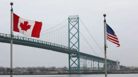 The Ambassador Bridge between Windsor, Canada and Detroit, Michigan, with Canadian and US flags in the foreground