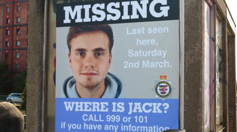 A large missing poster for Jack O'Sullivan, close to where he was last seen. The poster features a picture of him staring straight into the camera, in what appears to be a passport or ID picture. He is wearing a light blue hoodie, and has light brown hair. 