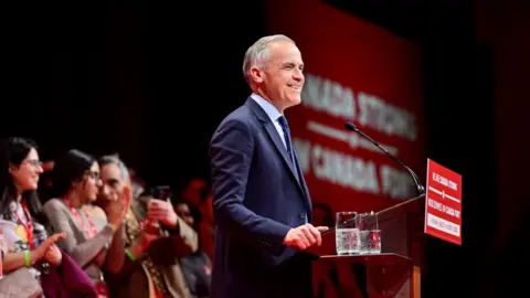 Mark Carney smiles wearing a suit behind a podium. 