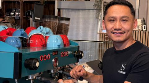 Shyam Lama stood next to a green coffee machine.