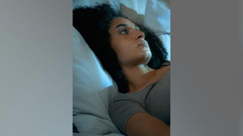 A woman with dark hair lies in bed